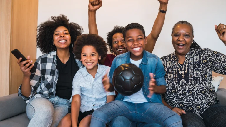 Gen Z black family sitting on a couch together cheering on a soccer game on tv