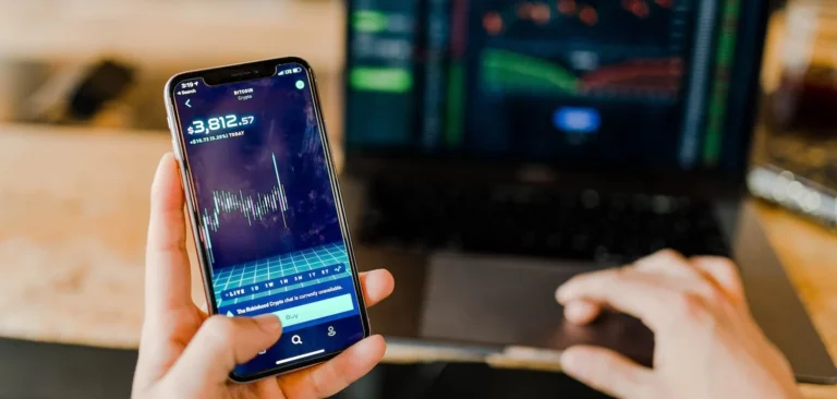 A hand holding a mobile phone with a stock ticker on the screen