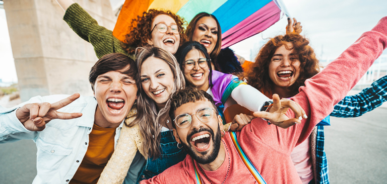 Group of LGBTQ+ Gen Z adults smiling under a pride flag