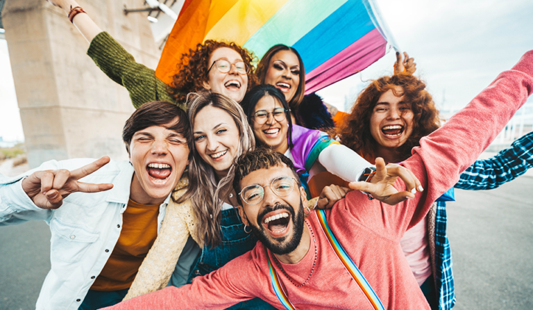 Group of LGBTQ+ Gen Z adults smiling under a pride flag